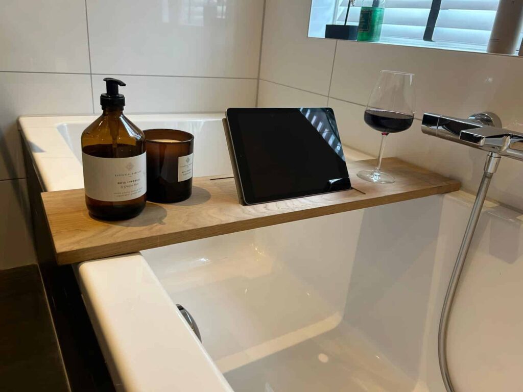 Badplank met RVS-plaat over een bad, met een tablet rechtop, een zeeppompje, een kaars en een glas rode wijn
