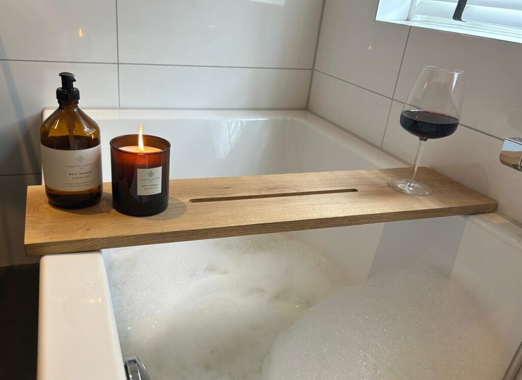 Badplank over een bad met schuim, met een zeeppompje, een brandende kaars en een glas rode wijn